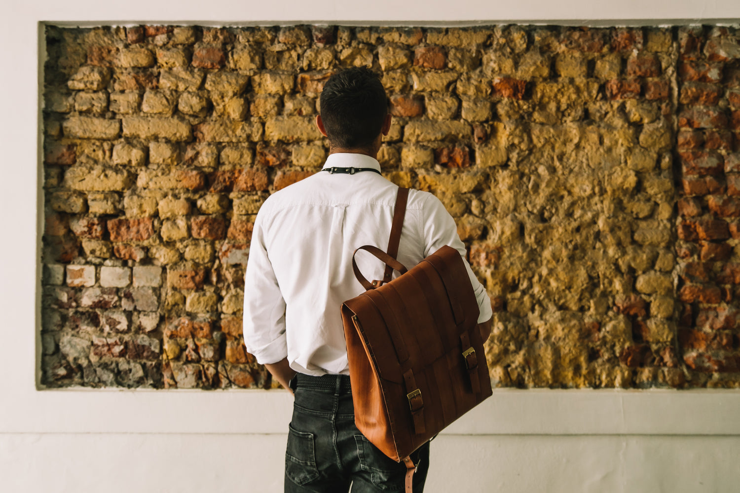 Man standing in front of brick wall with leather backpack 