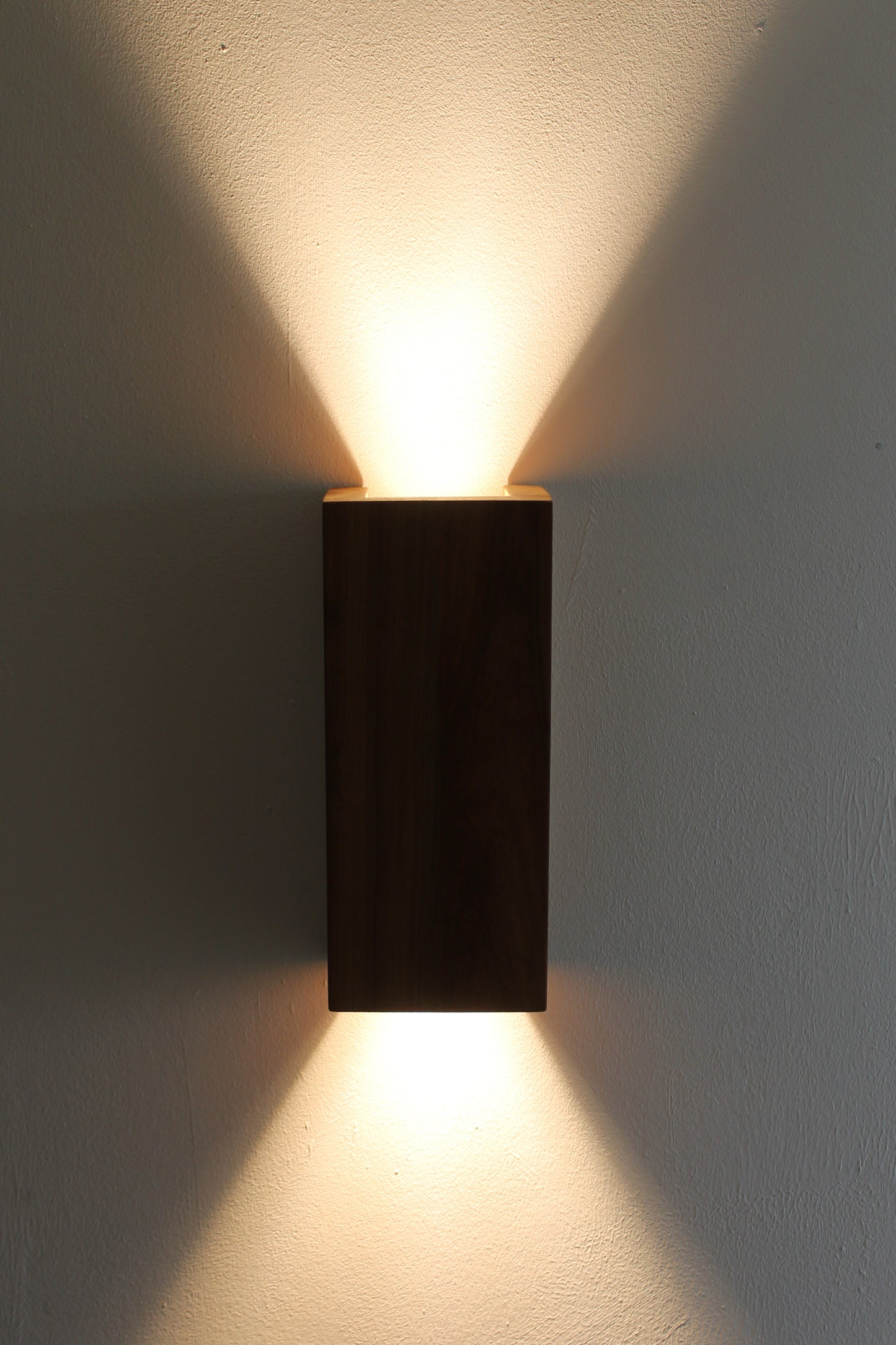 Wooden Up Down Wall Light illuminated in a dark room front view